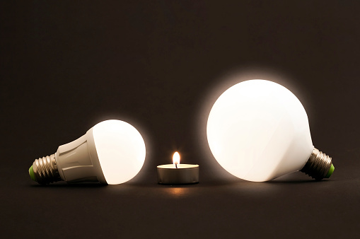White little candle and LED electric bulbs on dark background. Concept describing the evolution of lighting and energy saving.