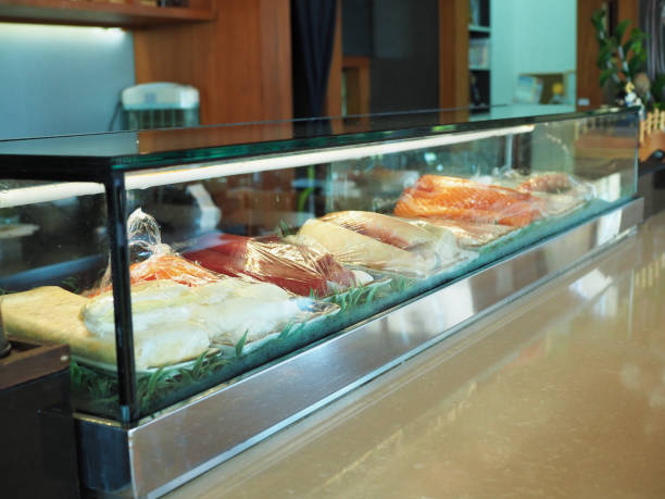 Counter Japanese sushi bar contain fresh raw fish such as salmon, tuna, hamachi  and kani in glass window refrigerator.