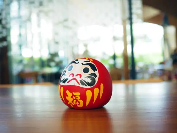 Photo of Daruma doll, a handmade Japanese doll symbolized of fortune or good luck place on wooden table.