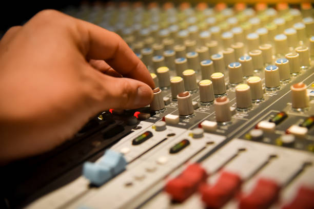 istock close-up hands of sound engineer adjusting audio mixer controller for live music and studio equipment. This is a quality audio system for professionals. vintage tone & effect light in control room. 958710500