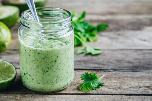 green salad dressing with avocado, lime and cilantro in a glass jar on a rustic background