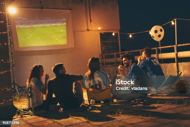 Group Of Friends Watching Football On A Building Rooftop Stock Photo - Download Image Now