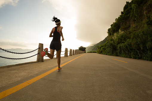 Sporty fitness woman running on sunrise seaside trail