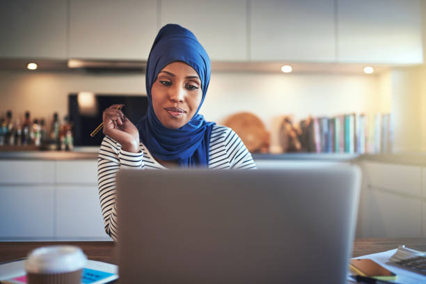 молодая арабская женщина-предпринимательница использует ноутбук на кухне - women middle eastern ethnicity islam hijab стоковые фото и изображения
