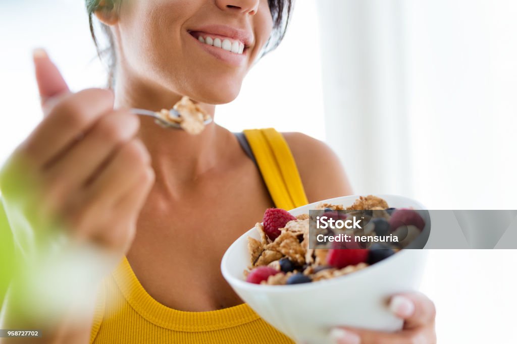 Bella giovane donna che mangia cereali e frutta a casa. - Foto stock royalty-free di Alimentazione sana