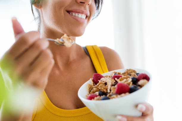 bella giovane donna che mangia cereali e frutta a casa. - adult muscular build athlete beautiful foto e immagini stock