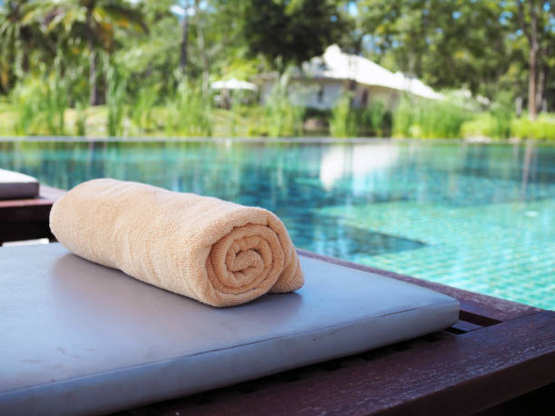 A close-up shot of neatly rolled towels placed on a wooden table by the poolside, creating a holiday concept.