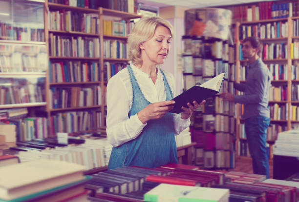 istock Glad woman reading book in book shop 958731370