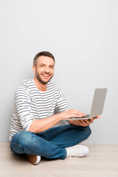 istock Cheerful happy smiling man sitting on floor with laptop 958737676