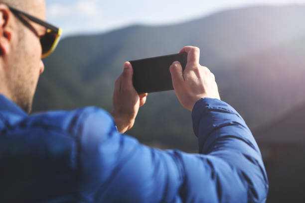 Woman hands holding a mobile phone at sunset golden hour and taking picture