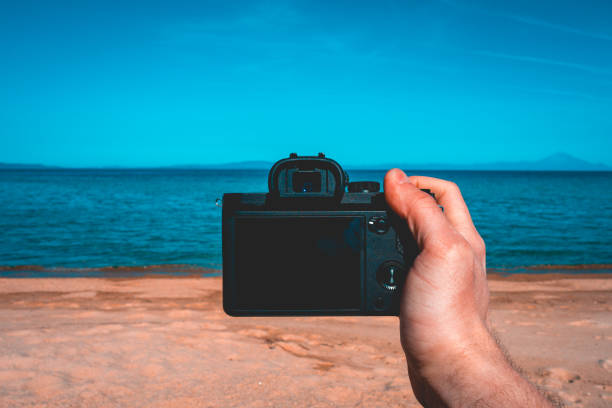 istock hand holding a camera on clean beach or holiday scene 958765562