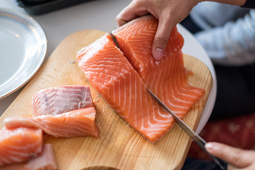 Hand chef using knife slice raw salmon on chopping block