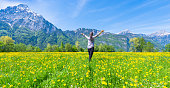 Woman with open hands on the field of flowering dandelions. Summer landscape against the background of mountains.
