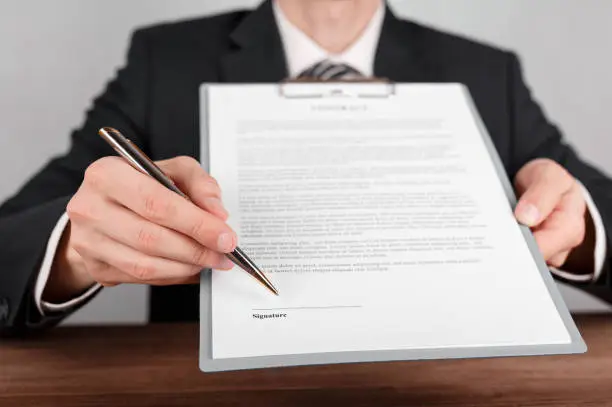 Photo of Businessman indicates the place for signing in the contract,which is attached to a clipboard.