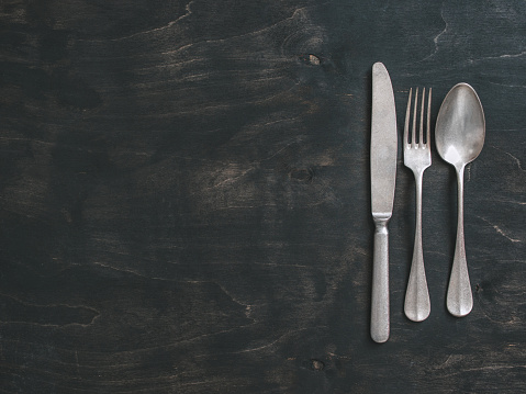Vintage cutlery over dark background. Old tablespoon, fork and knife on black table. Top view or flat-lay. Copy space for text.
