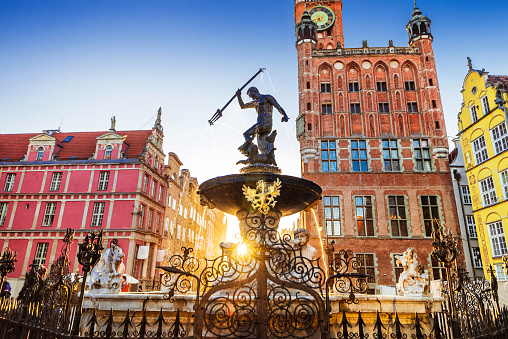 A panoramic view of Castle Square (Plac Zamkowy) in Warsaw, Poland. The image captures the various landmarks, buildings, and restaurants that make up the square. Notably, on the right side of the photo, Zamek Królewski w Warszawie (Royal Castle in Warsaw) is clearly visible. The facades of the buildings exhibit the architectural style of the area. People can be seen leisurely strolling along the square, adding a sense of activity to the scene. The sky above is adorned with a vibrant blue hue, with scattered clouds indicating a pleasant summer day. This photo provides an accurate representation of the significant landmarks, diverse buildings, bustling restaurants, and the presence of Zamek Królewski w Warszawie in Castle Square, Warsaw, Poland.