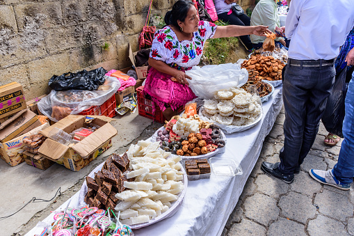 Santiago Sacatepequez, Guatemala - November 1, 2017: Local Maya woman dressed in traditional clothing sells typical candies in the street during the giant kite festival on All Saints' Day.
