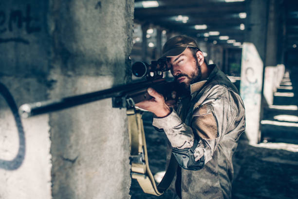 istock Calm and quiet adult is looking through lens. He is taking aim. Guy is standing besides column and waiting. Young man is in a big hangar 958831412