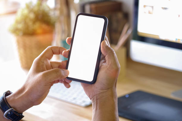 istock close-up man hand holding mobile phone showing blank screen and finger touching on work table. 958835520