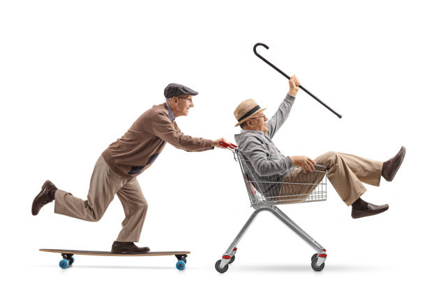istock Senior riding a longboard and pushing a shopping cart with another senior riding inside it 958840912
