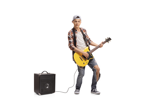 Full length portrait of a teenage boy with an electric guitar and an amplifier isolated on white background