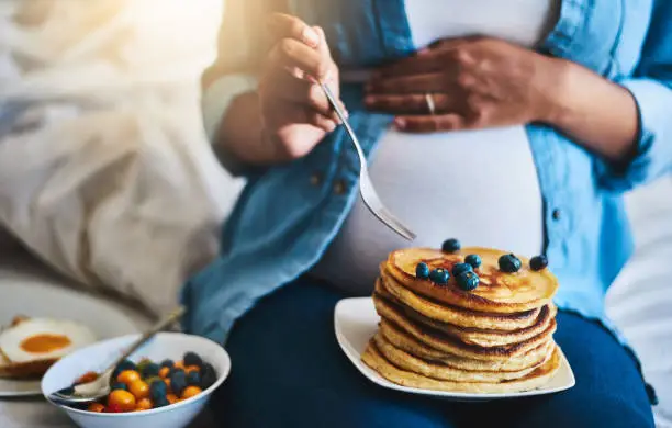 Cropped shot of a pregnant woman eating delicious pancakes at home