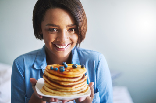 Shot of an attractive young woman eating delicious pancakes at home