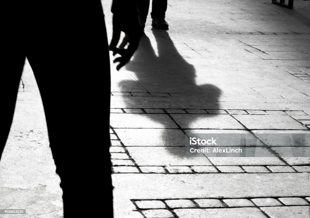 Silhouette shadow of two people Shadow silhouette of two person on city sidewalk in black and white Violence Stock Photo