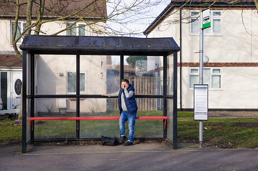 A boy with down syndrome uses a smartphone whilst waiting at the bus stop.