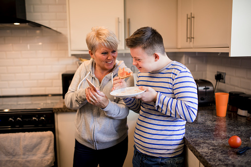 A boy with down syndrome eats toast whilst his mother shows him her smartphone.