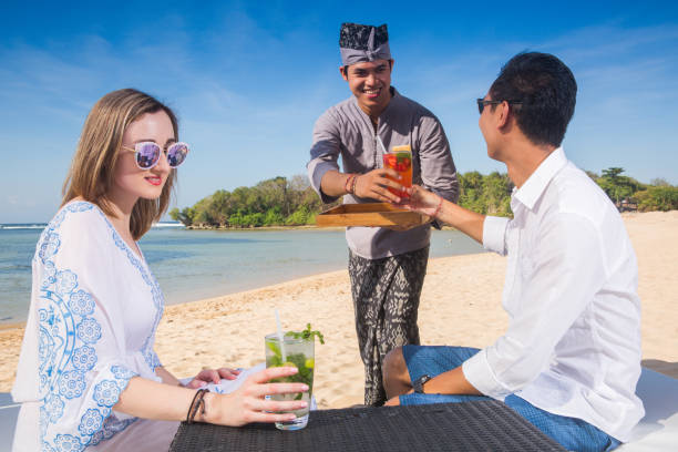 istock Couple on a tropical beach with cocktail drinks. Waiter serving drinks on beach. Ocean sea view 958874256