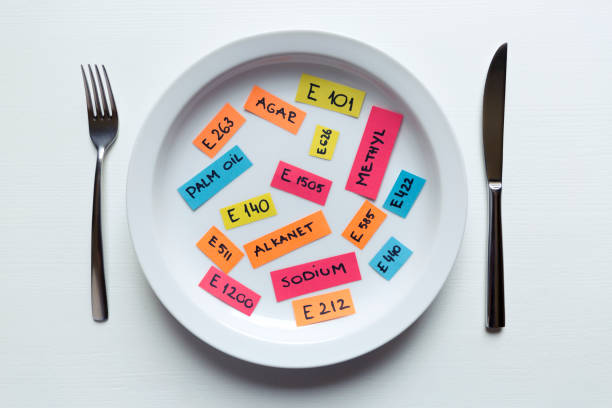 Colorful paper notes naming food additives on plate with fork and knife, food additive and unhealthy food concept. stock photo