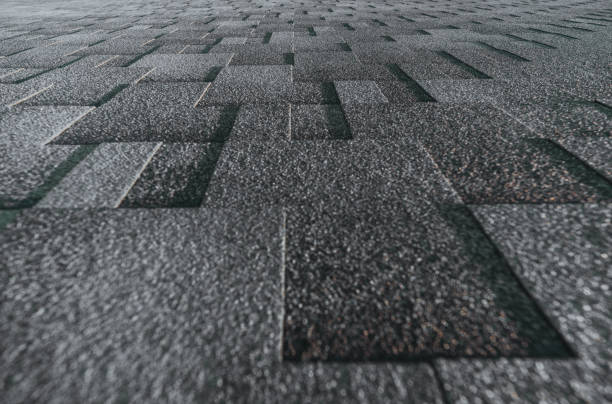 Soft roof tiled gray grainy texture on the top of a summer house lit by the sun; grey soft roofing tiles covering a building, focus on the middle distance