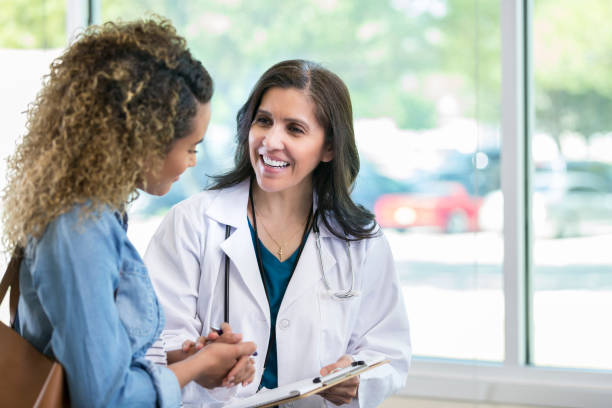 Female doctor discusses something with young mixed race patient Caring mature female doctor shows test results to a young adult female patient. The doctor is smiling while talking with the patient. lab coat photos stock pictures, royalty-free photos & images