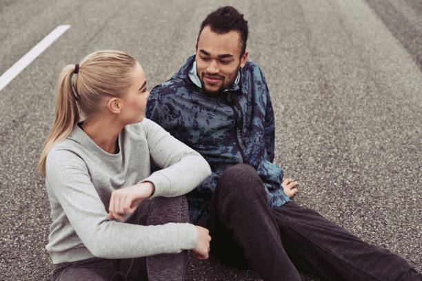 istock Young couple smiling while sitting on a road after jogging 958891020
