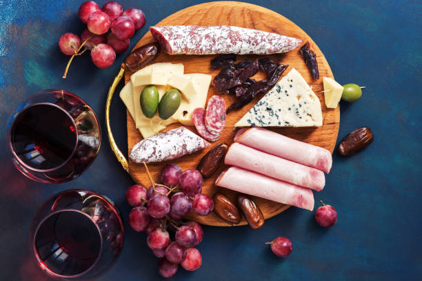 istock Delicious appetizers with red wine on a blue background. Fruit, cheese, ham, sausage. Top view, flat lay 958914752