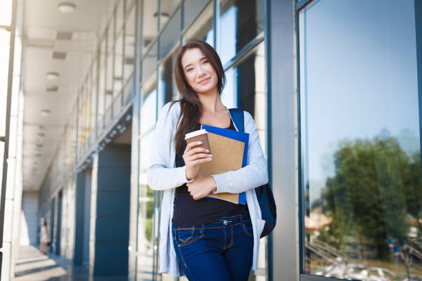 istock Young female IT student, with books and backpack. Staying outside before lesson and drinking coffee 958918112