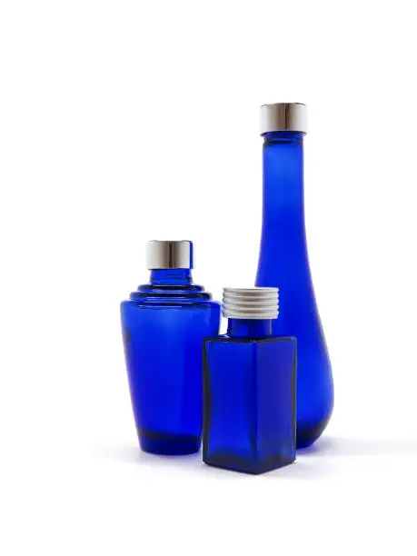 Blue glass bottles on white background. Three empty cobalt blue bottles with silver lids, each a different design. Glassware intended for cosmetics, oils, perfumes, lotions and potions. Vertical.