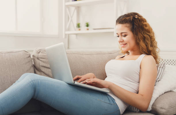 istock Young girl with laptop sitting on beige couch 958920502