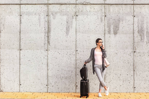 istock Young woman using her smart phone standing beside the concrete wall 958923132