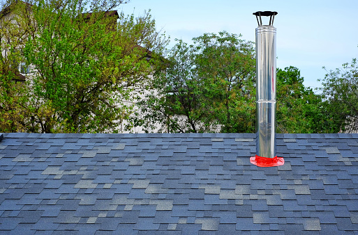 Close up view on bitumen asphalt roofing shingles and stainless steel chimney pipe. Individual heating system.