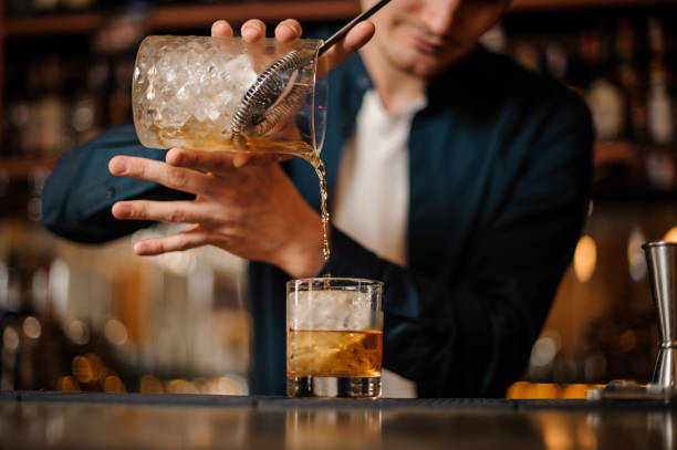 istock Brunet bartender pouring an alcoholic drink into a glass with a big ice cube 958937734
