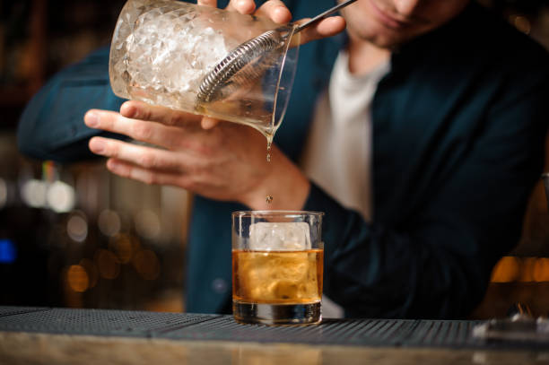 istock Brunet bartender pouring an alcoholic drink into a glass with an ice cube 958940060