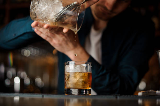 istock Bartender pouring an alcoholic cocktail into a glass with a big ice cube 958940100