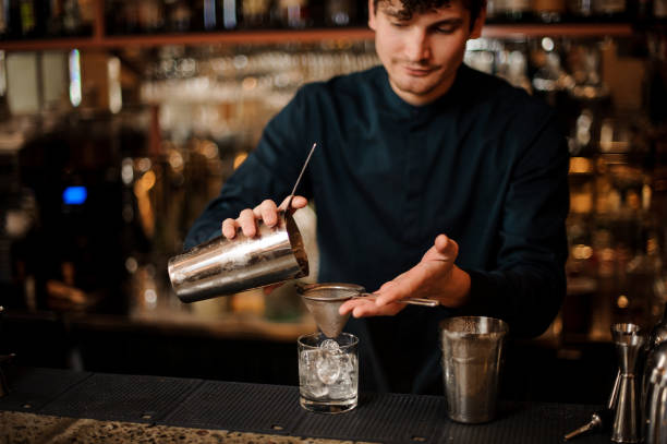 istock Bartender pouring an alcoholic cocktail into a glass from a steel shaker 958940164