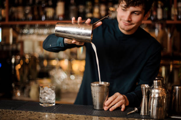 istock Smiling brunette bartender pouring an alcoholic cocktail into a steel shaker 958940240