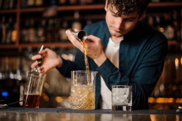 istock Brunet bartender pouring an alcoholic drink into the glass with ice 958940718