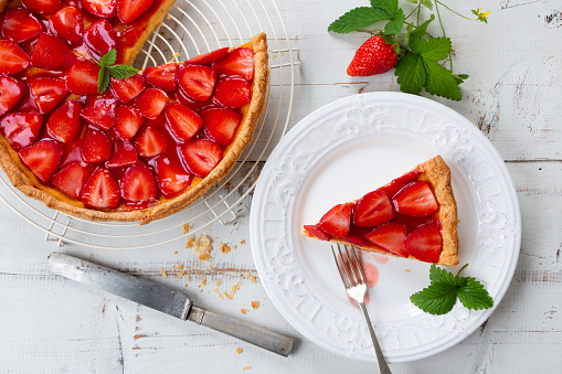 Homemade strawberry tart decorated with strawberry leaves and portion in a plate. Top view