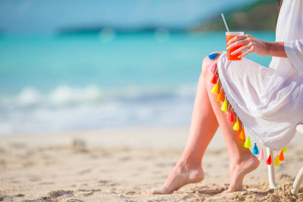 Young woman with cocktail glass on white beach sitting on sunbed. Closeup tasty cocktail background the sea