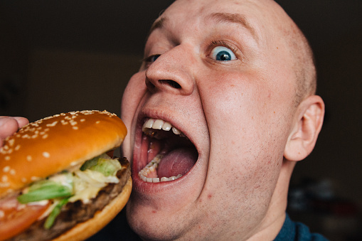 The eating of a hamburger by a man with a terrible expression.